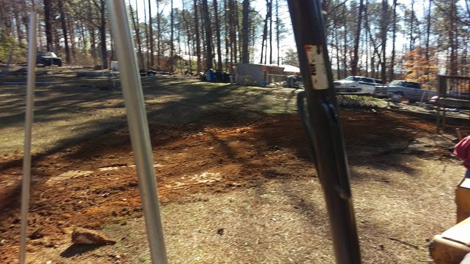 Wooded residential yard with freshly graded red dirt covering a completed septic system repair near Birmingham, Alabama.