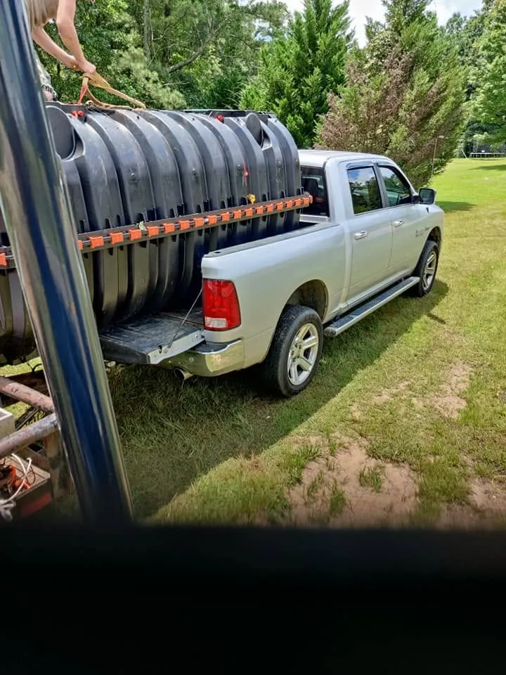 Stacked black plastic drain field chambers strapped into the bed of a silver pickup truck parked on grass.