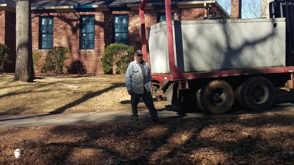 Worker standing beside a truck carrying a precast concrete septic tank in front of a brick house.