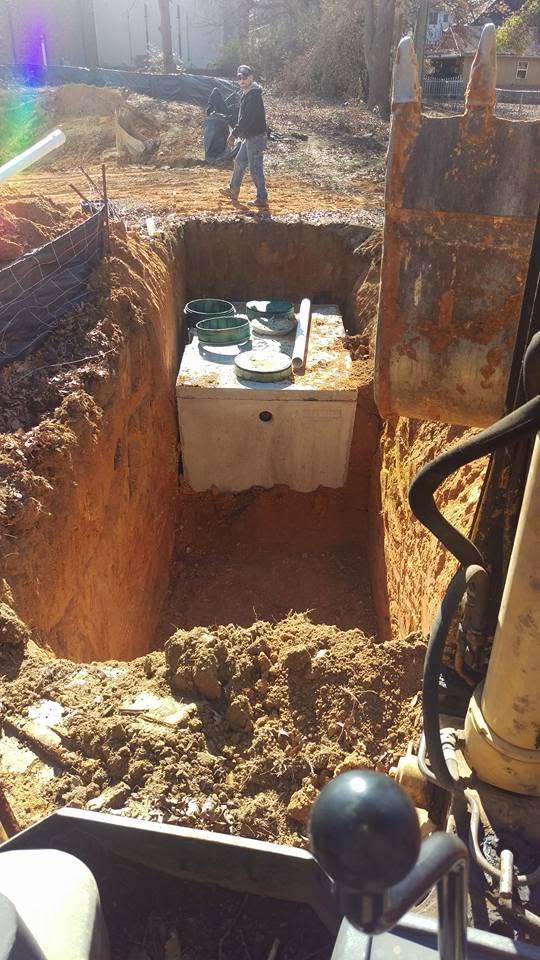 View from excavator of a concrete septic tank with green risers set in a deep red clay excavation pit.